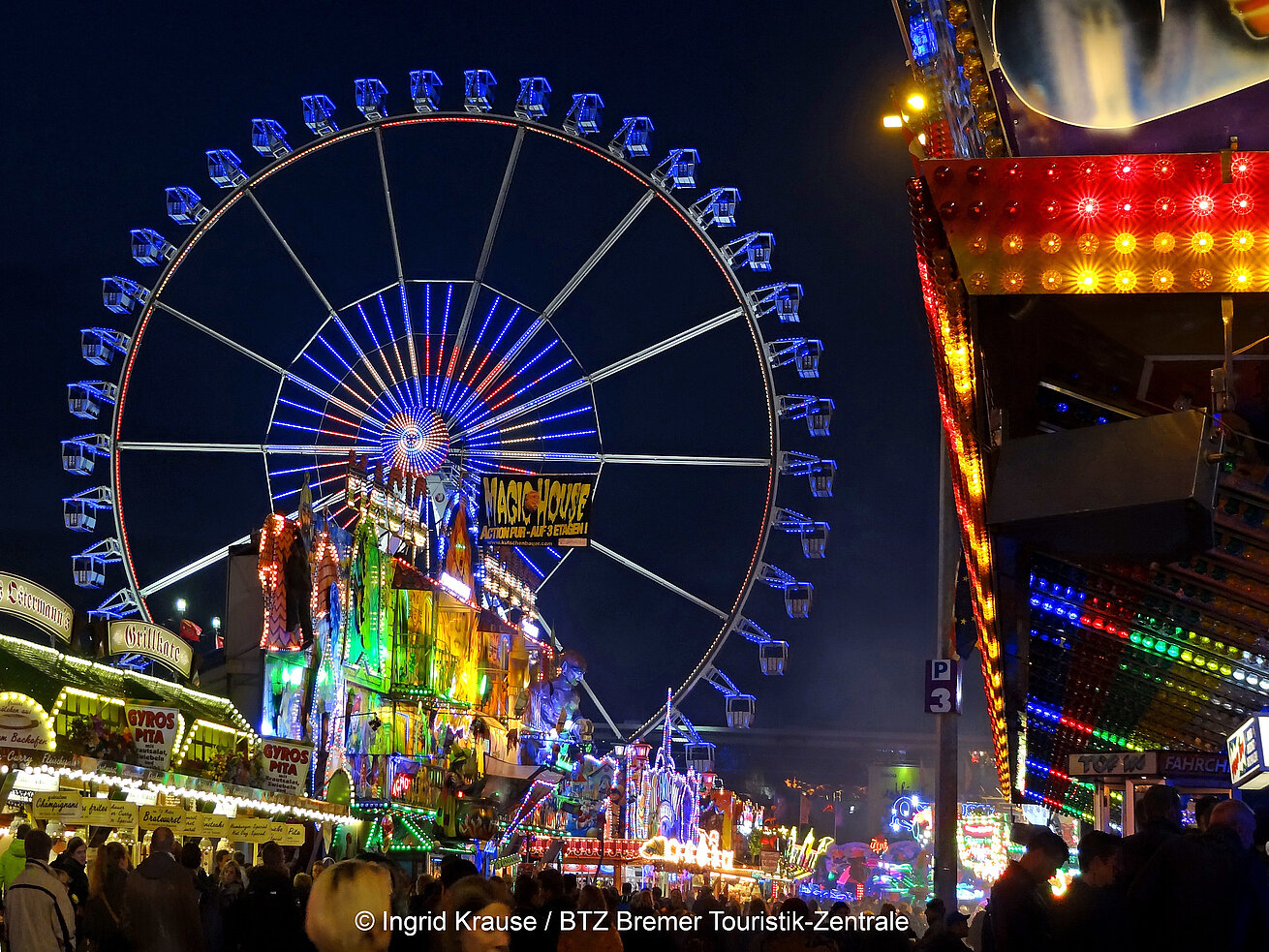 Ferris wheel and colourful rides at Bremen Freimarkt fair at night with many visitors