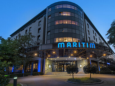 Exterior view of Maritim Hotel Bremen at dusk, illuminated logo and modern architecture.