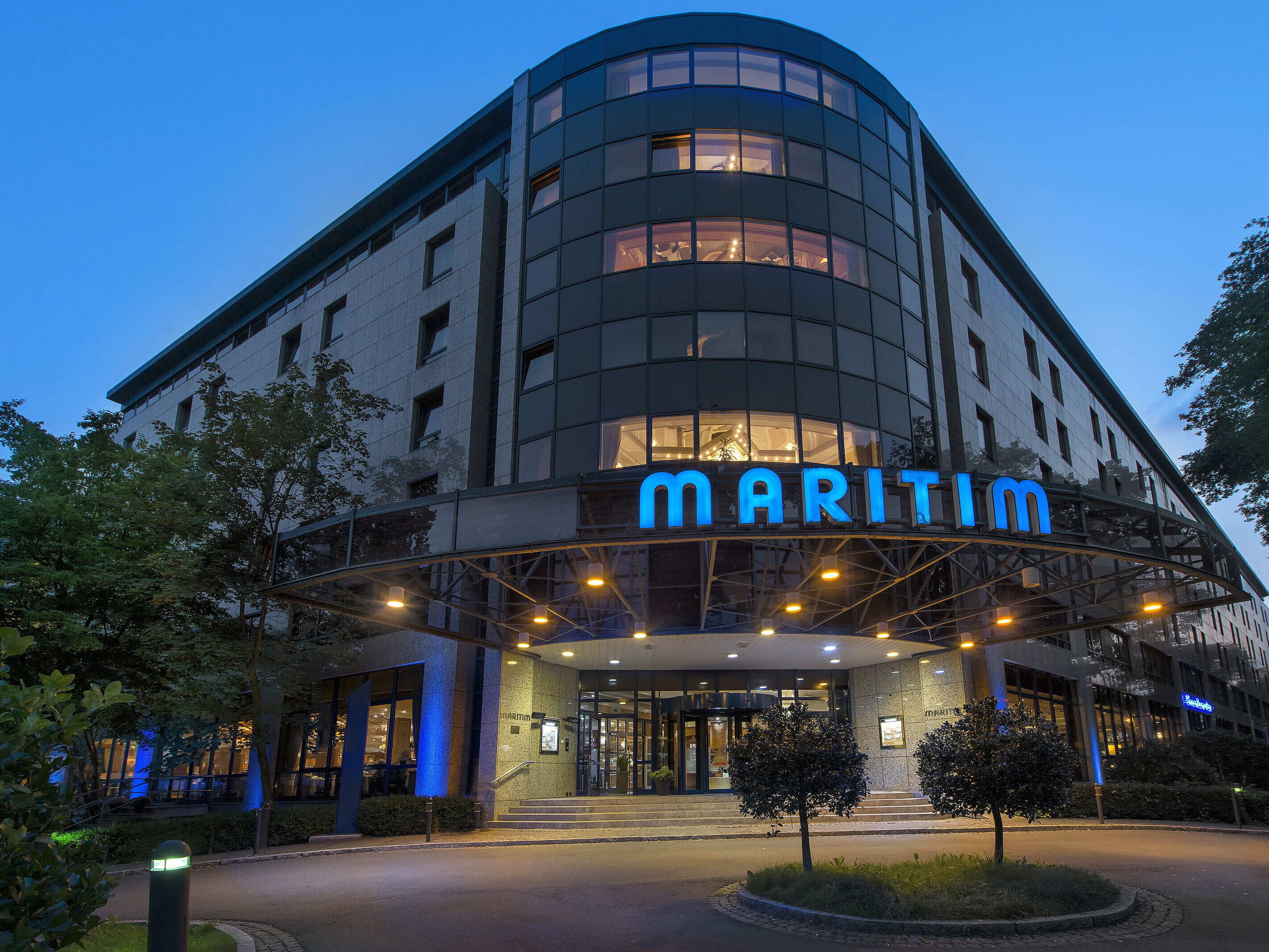 Exterior view of Maritim Hotel Bremen at dusk, illuminated logo and modern architecture.