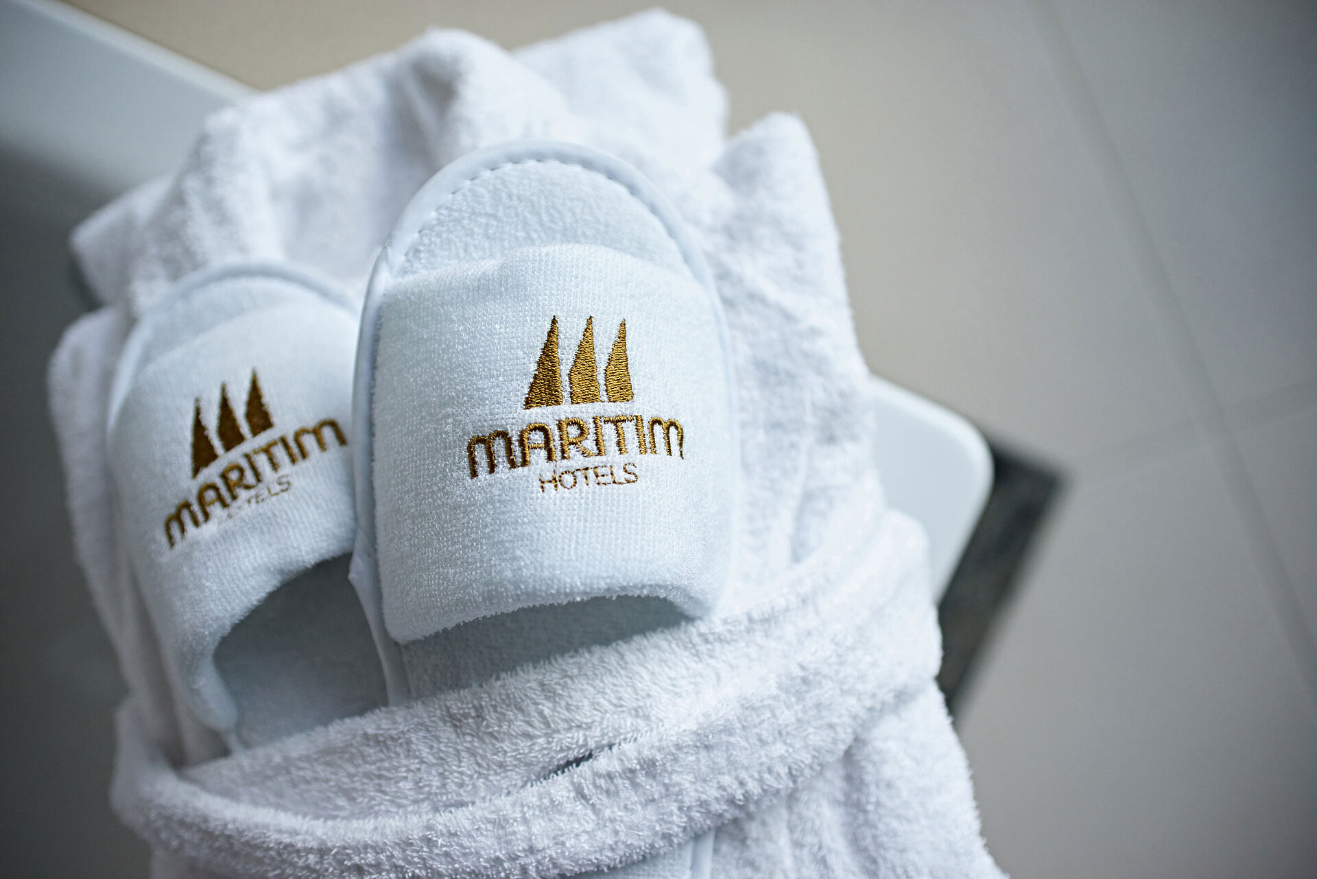White Maritim Hotels slippers placed on a folded bathrobe, conveying a relaxing spa atmosphere.