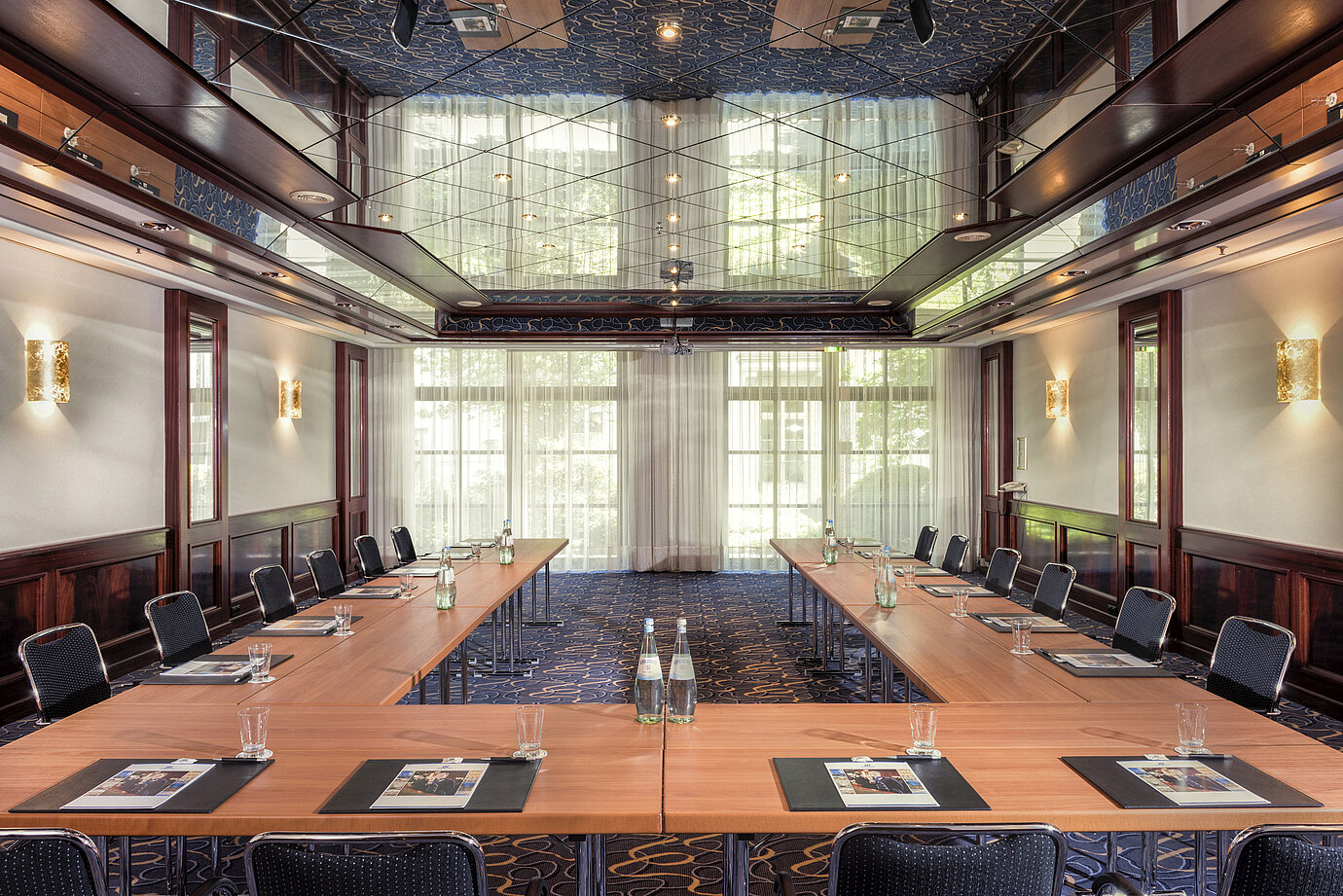 Stylish conference room with U-shaped seating, natural light, and an elegant mirrored ceiling.