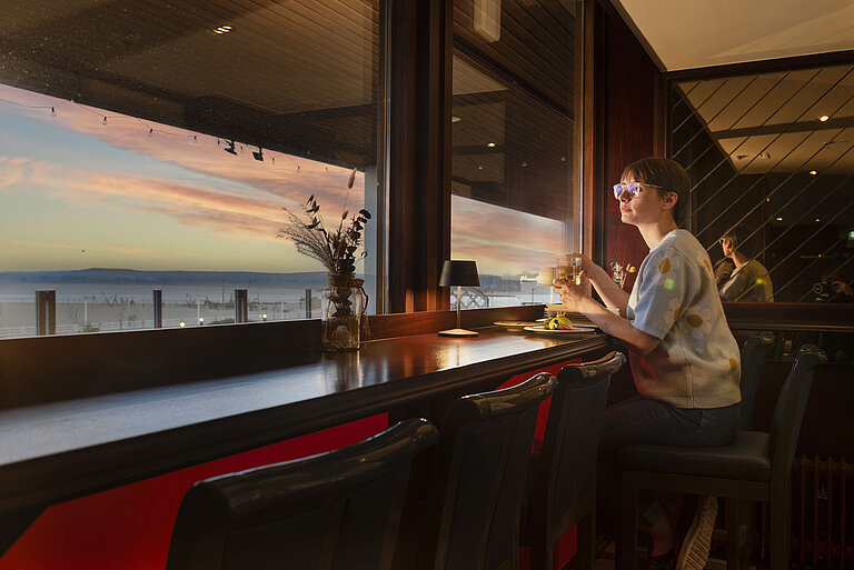 Guest enjoying a drink by the window with a sunset view at Maritim Hotel Travemünde