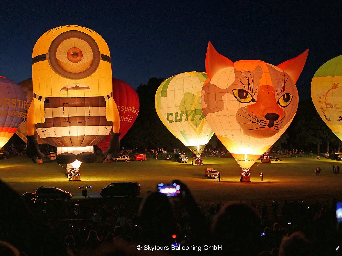 Illuminated hot air balloons during a night glow event with spectators