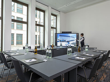 Compact meeting room at Maritim Hotel Ingolstadt with large screen, modern technology, and natural light.