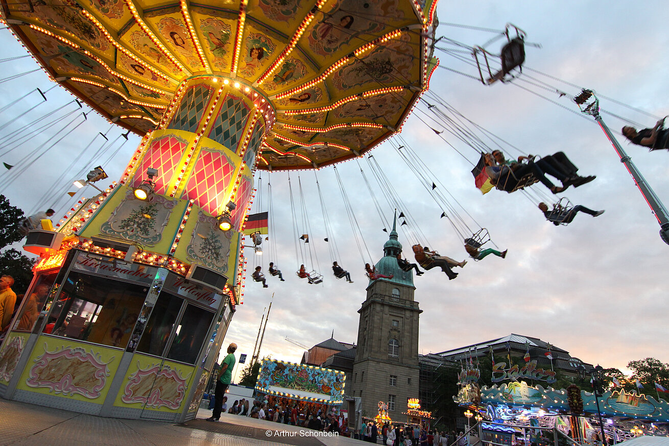 Swing carousel ride at fairground with illuminated rides during evening