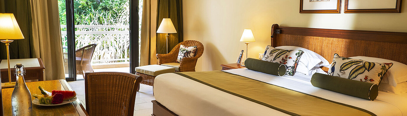 Elegant hotel room with balcony, desk, seating area and green surroundings