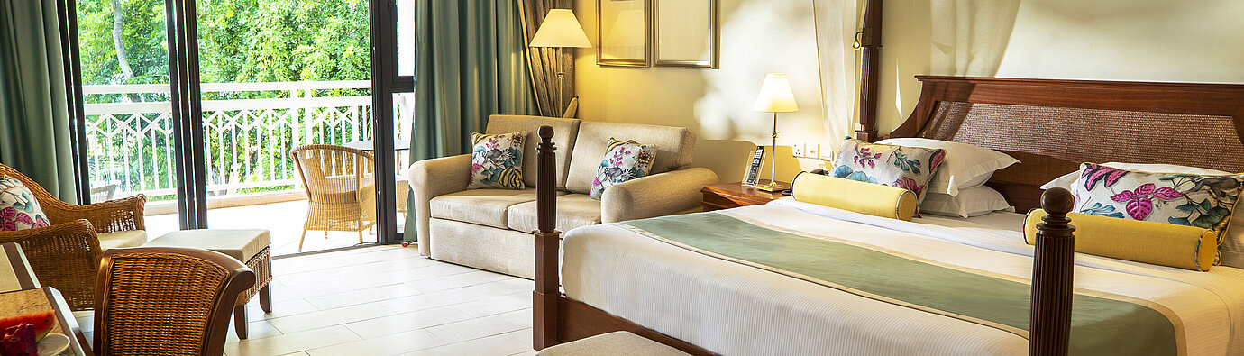 Spacious hotel room with four-poster bed, sofa, balcony and green views