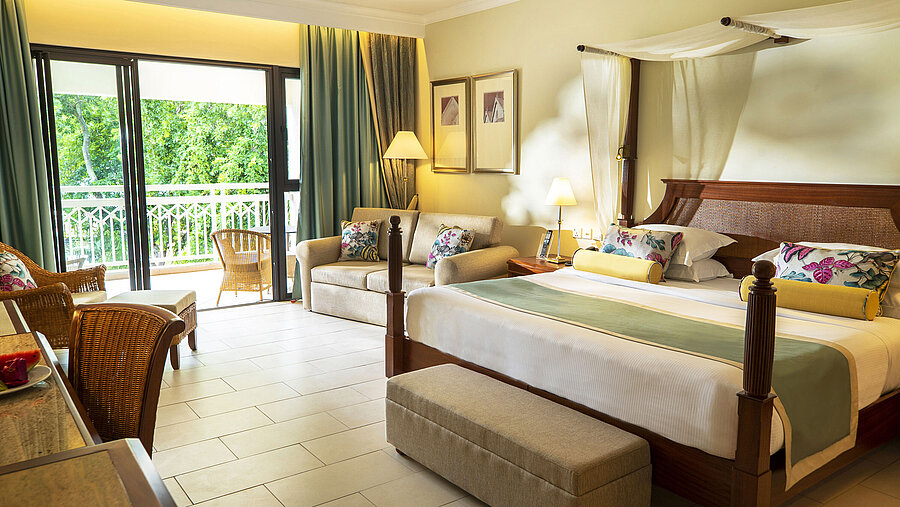 Spacious hotel room with four-poster bed, sofa, balcony and green views