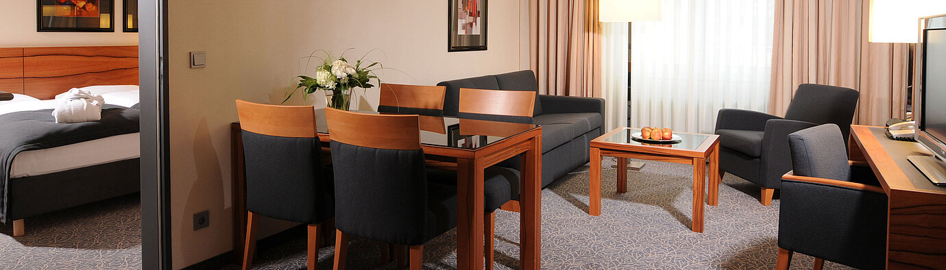 Spacious suite with living room, dining table and separate bedroom at Maritim Hotel Munich