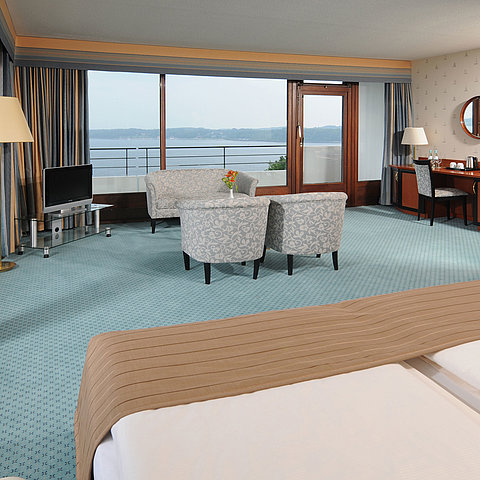 Junior Suite in the Maritim Hotel Kiel, with sitting area, desk, TV and large window front with sea view.