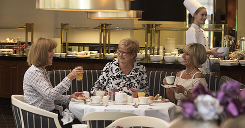 Three women enjoying a relaxed breakfast at Maritim Hotel Bad Homburg, served by a friendly chef.