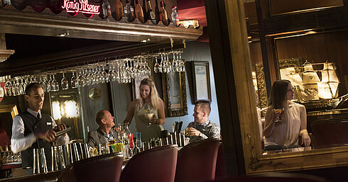 Atmospheric bar at the Maritim Hotel Kiel with guests enjoying cocktails while the bartender mixes a drink.