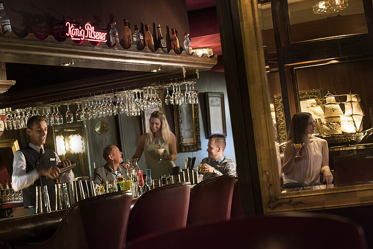 Atmospheric bar at the Maritim Hotel Kiel with guests enjoying cocktails while the bartender mixes a drink.