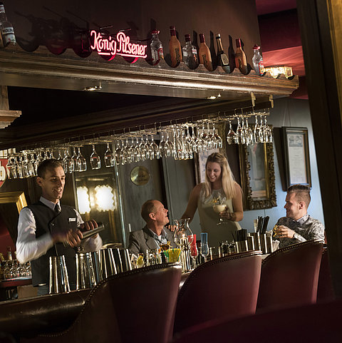 Atmospheric bar at the Maritim Hotel Kiel with guests enjoying cocktails while the bartender mixes a drink.