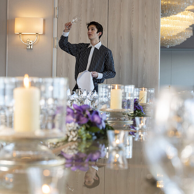 Staff in the Salon Oslo at the Maritim Hotel Kiel examining a glass of wine, festively laid table with candles and floral decorations.