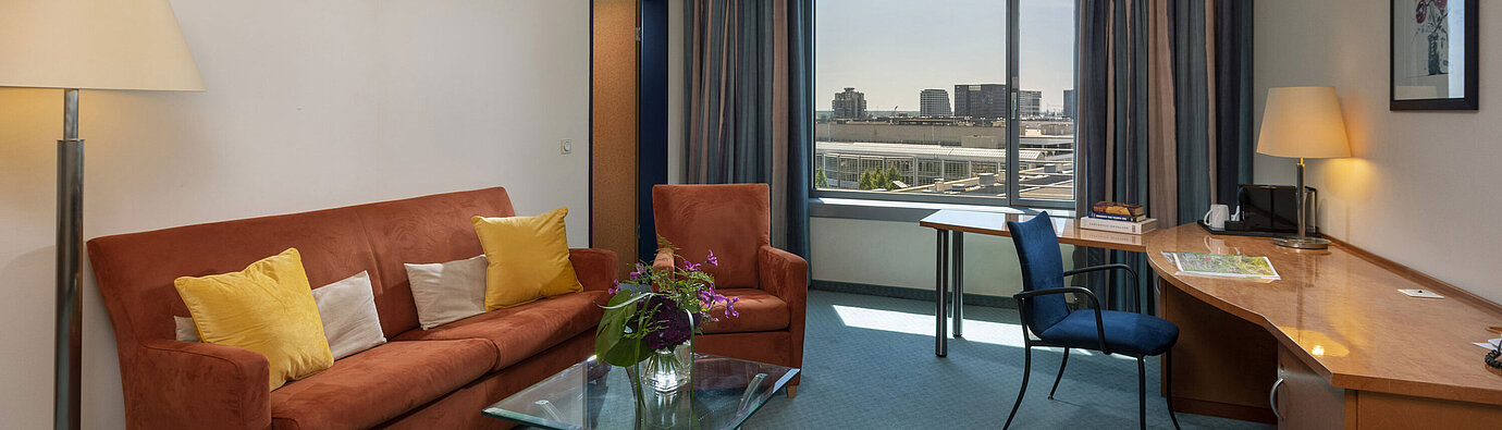 Junior Suite at Maritim Hotel Frankfurt with separate living area, sofa, desk, and panoramic city view.