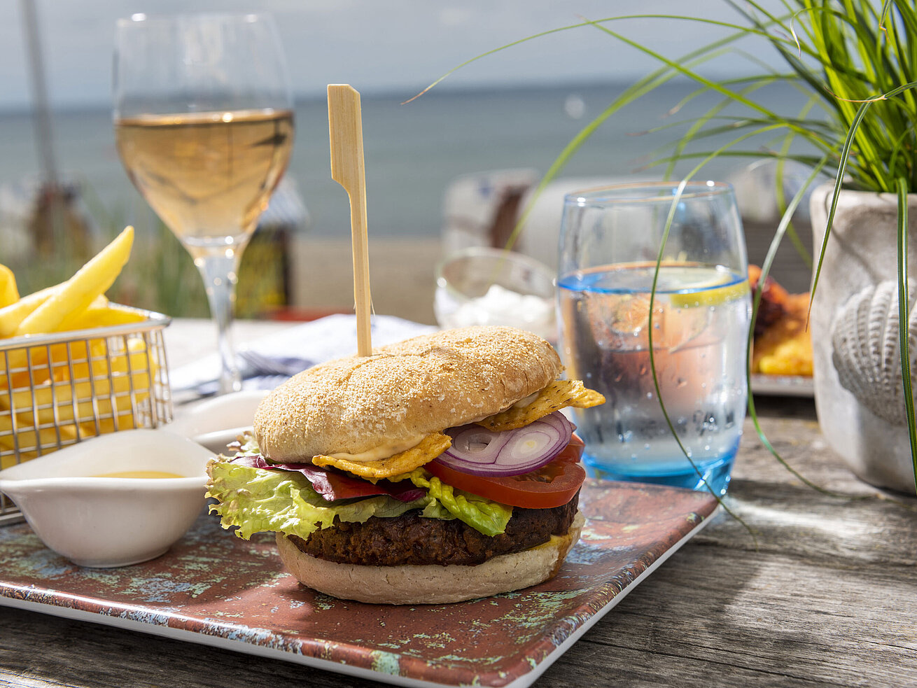 Burger with fries, salad and drinks on a wooden table in the beach lounge of the Maritim Hotel Timmendorfer Strand.