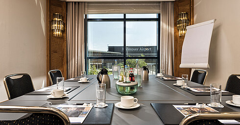 Bright meeting room with a conference table, drinks, and a view of the airport at Maritim Hotel Hannover.