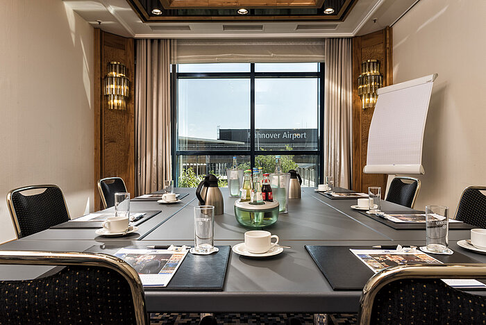 Bright meeting room with a conference table, drinks, and a view of the airport at Maritim Hotel Hannover.