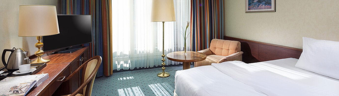 Bright Comfort room at Maritim Hotel Cologne with single bed, desk, TV, armchair, and large windows with curtains.
