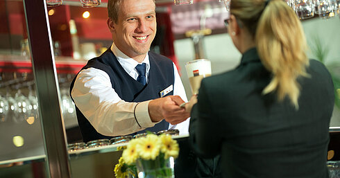A bartender handing a drink to a guest at the bar in Maritim Hotel with a friendly smile.