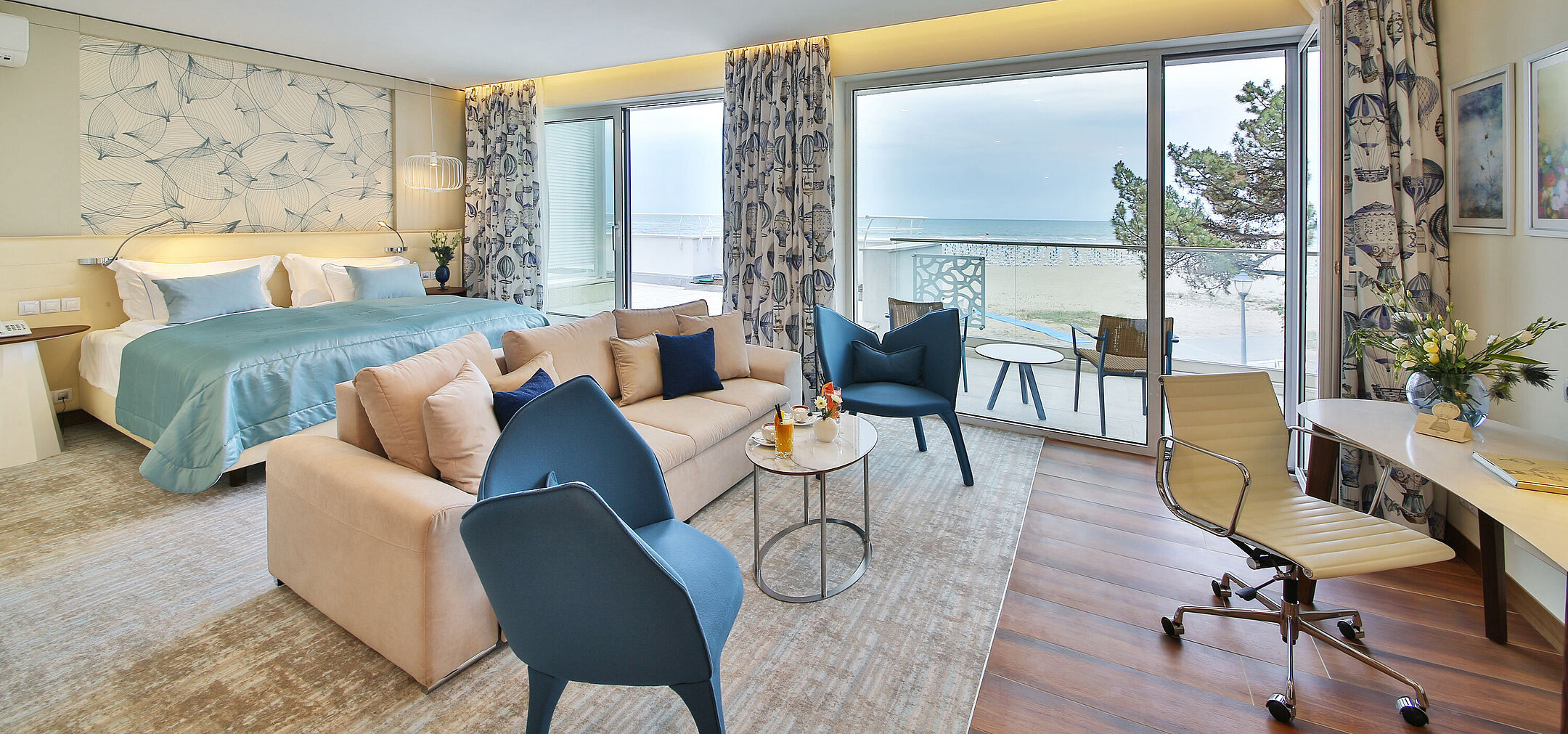 Suite with large bed, seating area and balcony with sea view in a modern hotel
