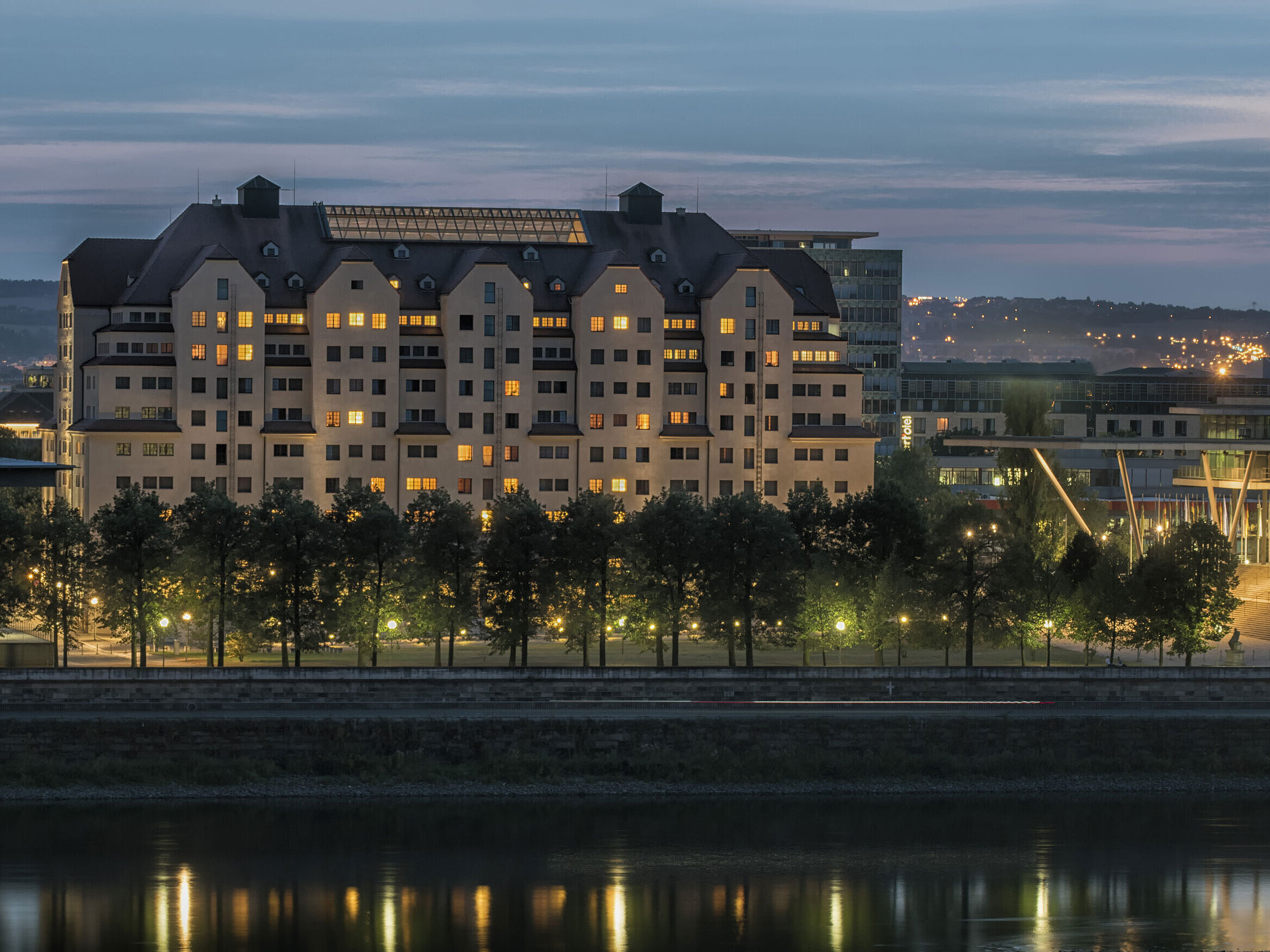 Illuminated Maritim Hotel Dresden at dusk with lights reflecting on the Elbe River.