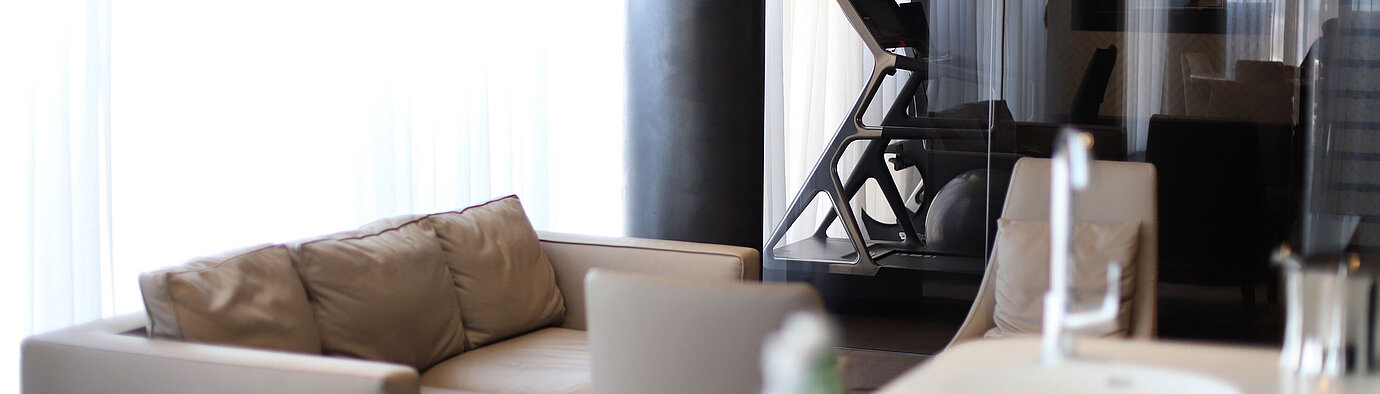Seating area with beige sofa and view of gym with treadmill behind glass at Maritim Hotel Plaza Tirana