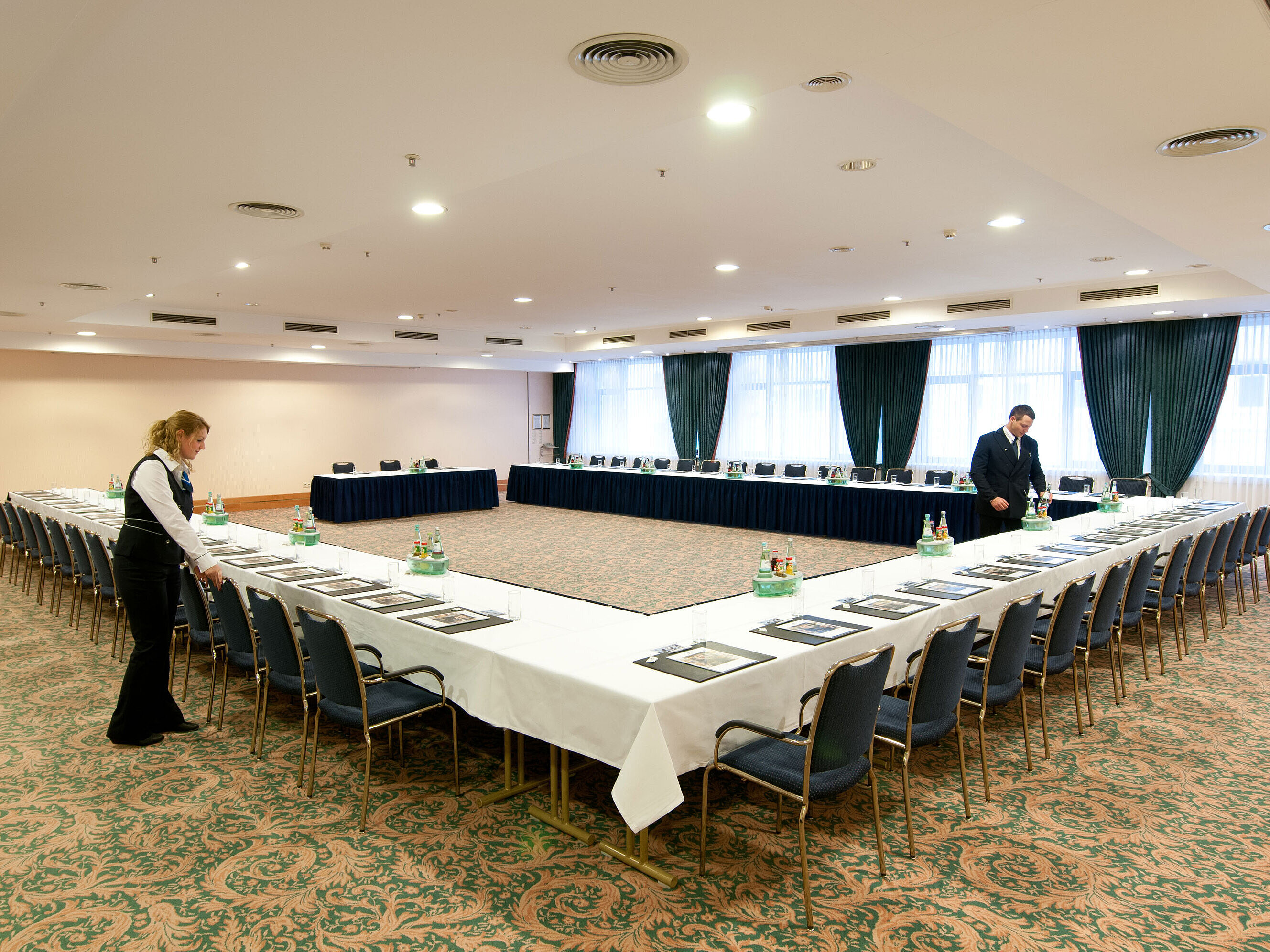 Conference room at Maritim Hotel Magdeburg with U-shaped seating, set tables, and staff preparations.