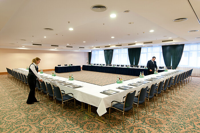 Conference room at Maritim Hotel Magdeburg with U-shaped seating, set tables, and staff preparations.