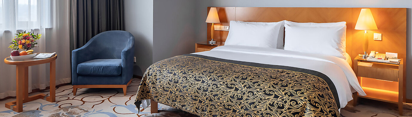 現代化酒店客房配備特大床、藍色扶手椅、落地窗景及暖色照明，營造舒適放鬆的住宿體驗