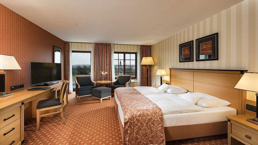 Superior room at Maritim Hotel Dresden with elegant double bed, desk, and seating area with city view.