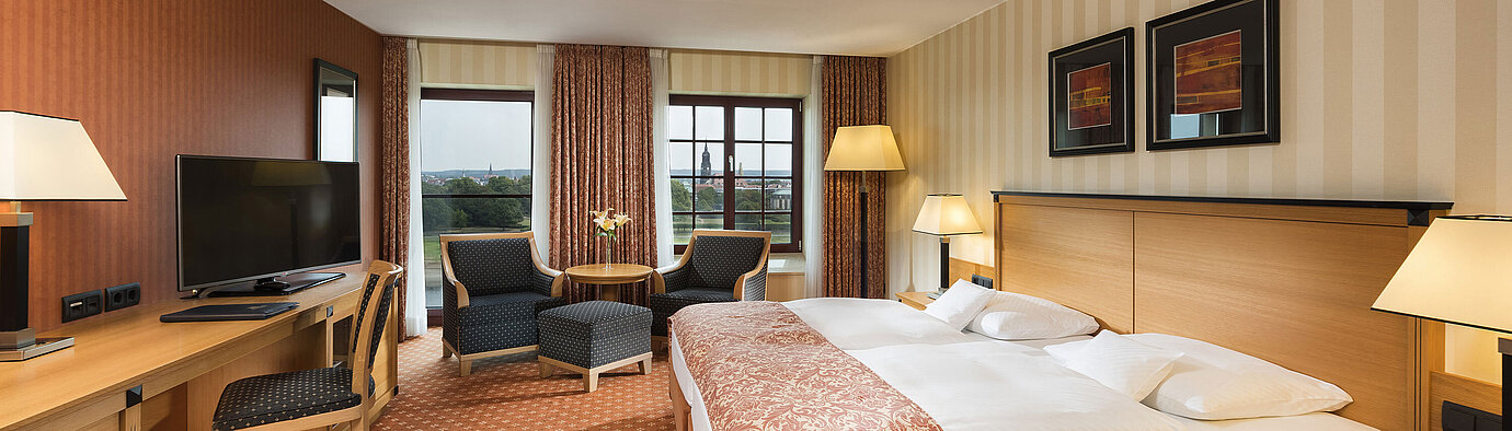 Superior room at Maritim Hotel Dresden with elegant double bed, desk, and seating area with city view.