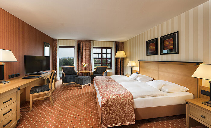 Superior room at Maritim Hotel Dresden with elegant double bed, desk, and seating area with city view.