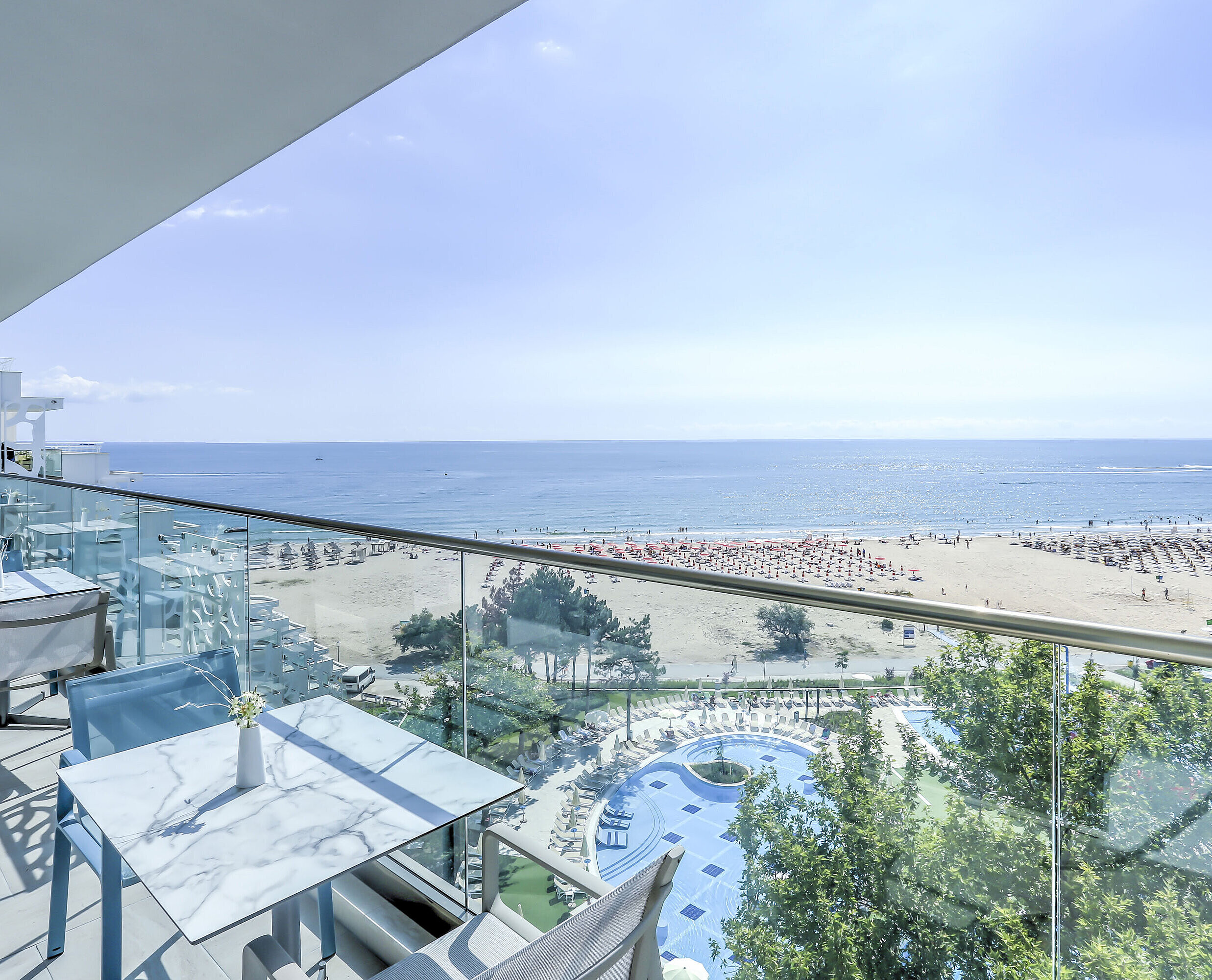 Balcony terrace with tables, glass railing and wide views of the beach, sea and resort pools