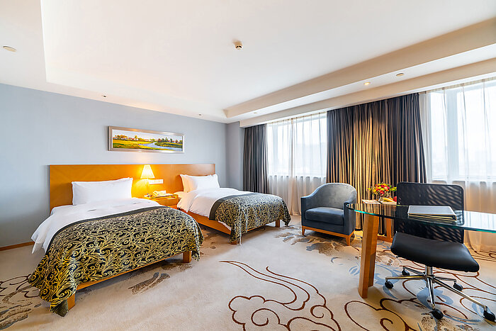 現代化酒店客房配備兩張單人床、大窗戶、藍色扶手椅及工作區，提供舒適住宿體驗
