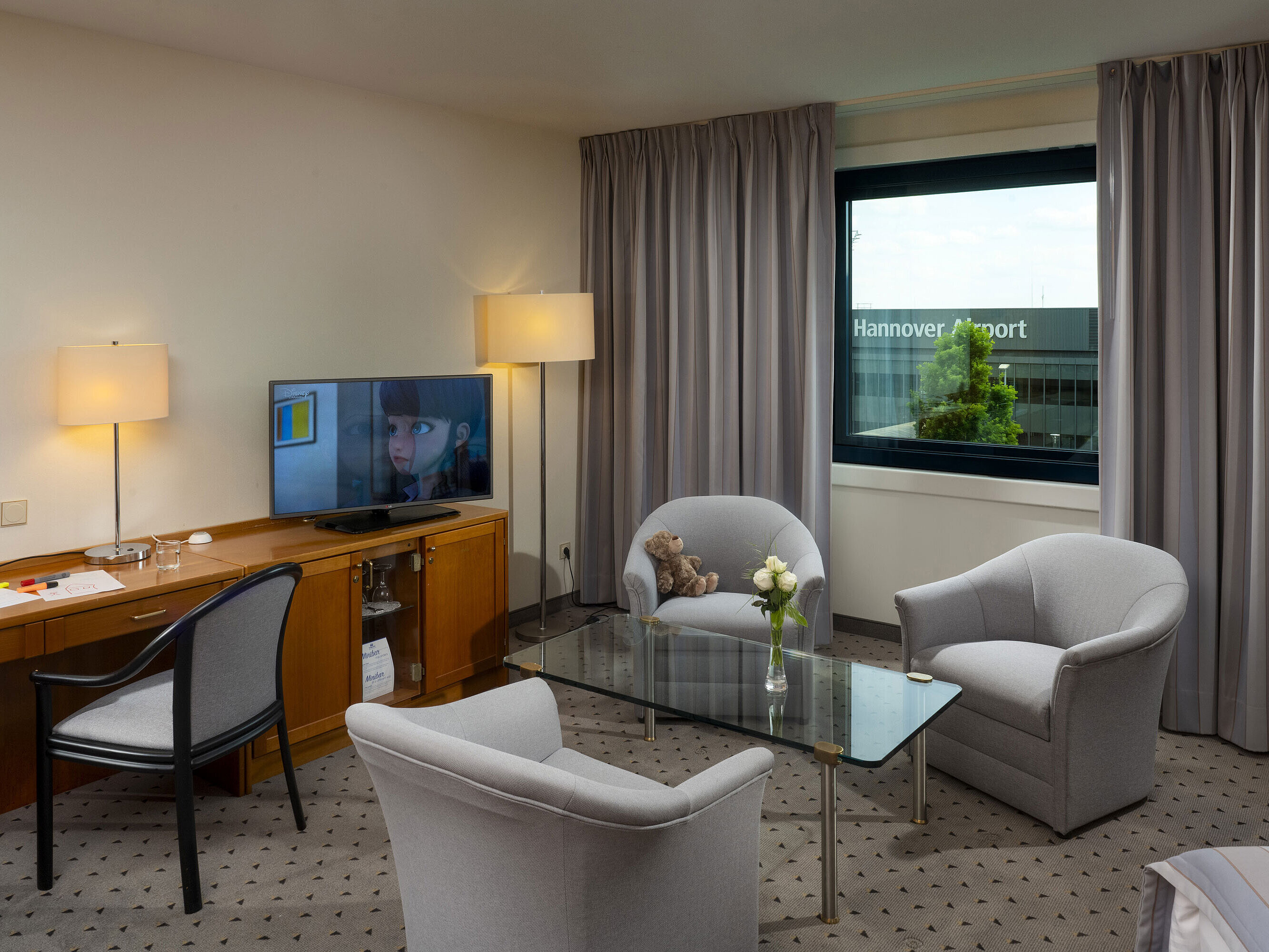 Comfortable family room with seating area, TV, and view of Hannover Airport at Maritim Hotel Hannover.