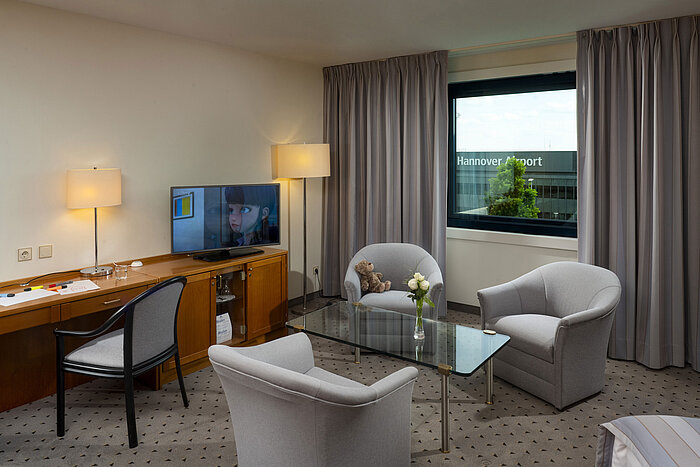 Comfortable family room with seating area, TV, and view of Hannover Airport at Maritim Hotel Hannover.