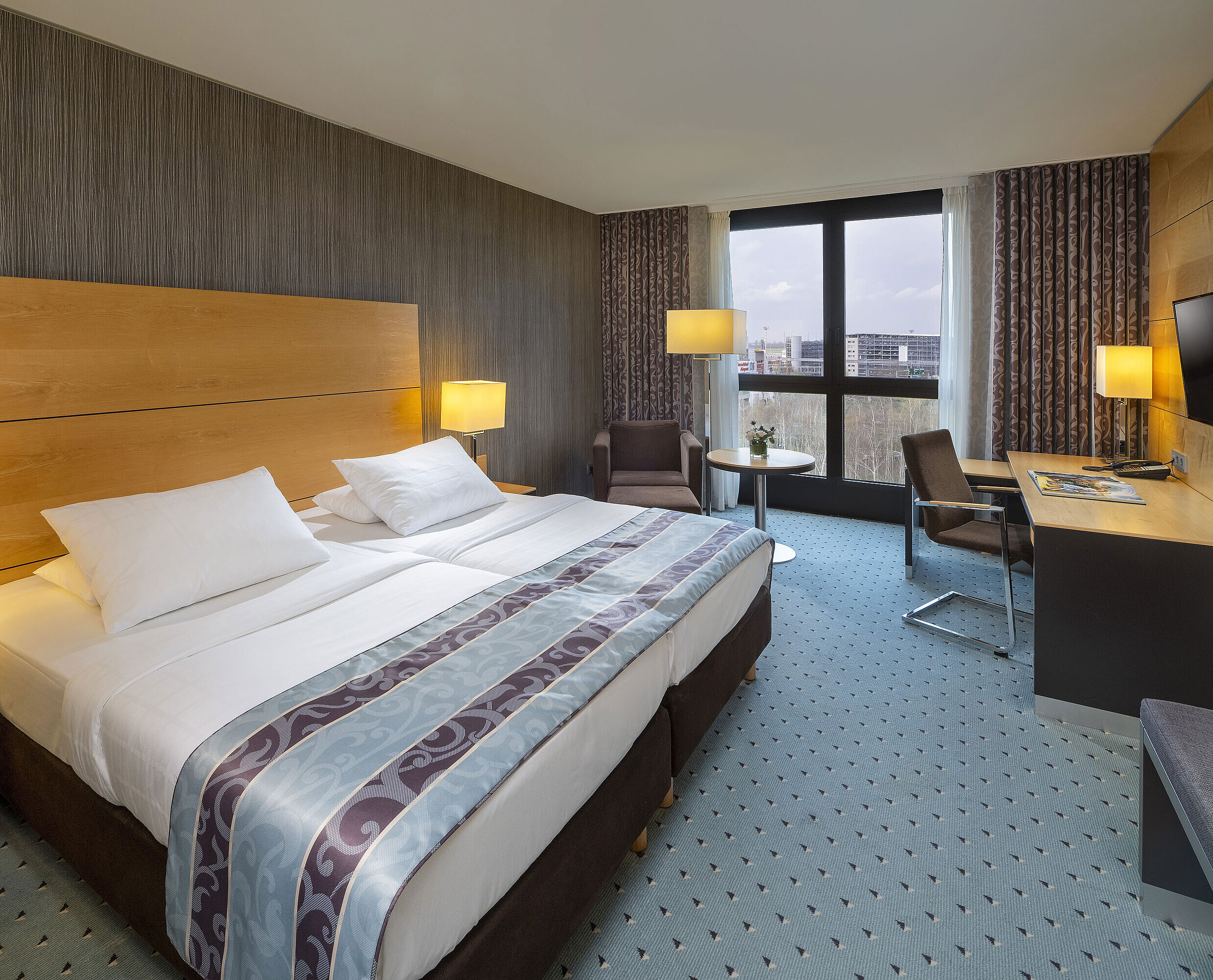 Comfort room at Maritim Hotel Düsseldorf with a large double bed, desk, armchair, and panoramic window.