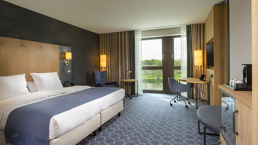 Spacious double room at Maritim Hotel Ingolstadt with bed, desk, and a view of the river.
