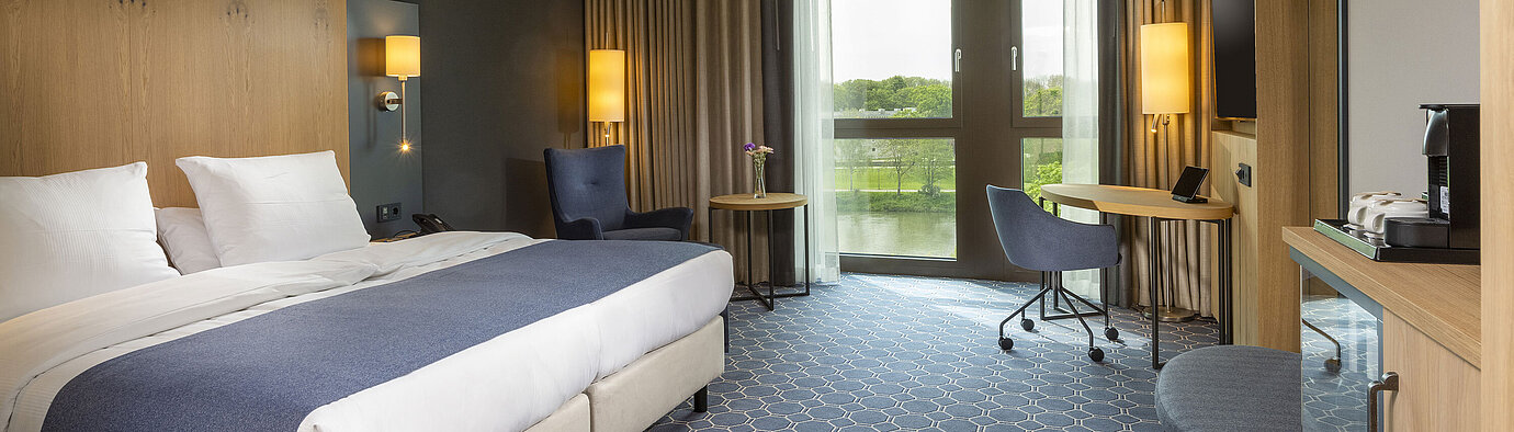 Spacious double room at Maritim Hotel Ingolstadt with bed, desk, and a view of the river.