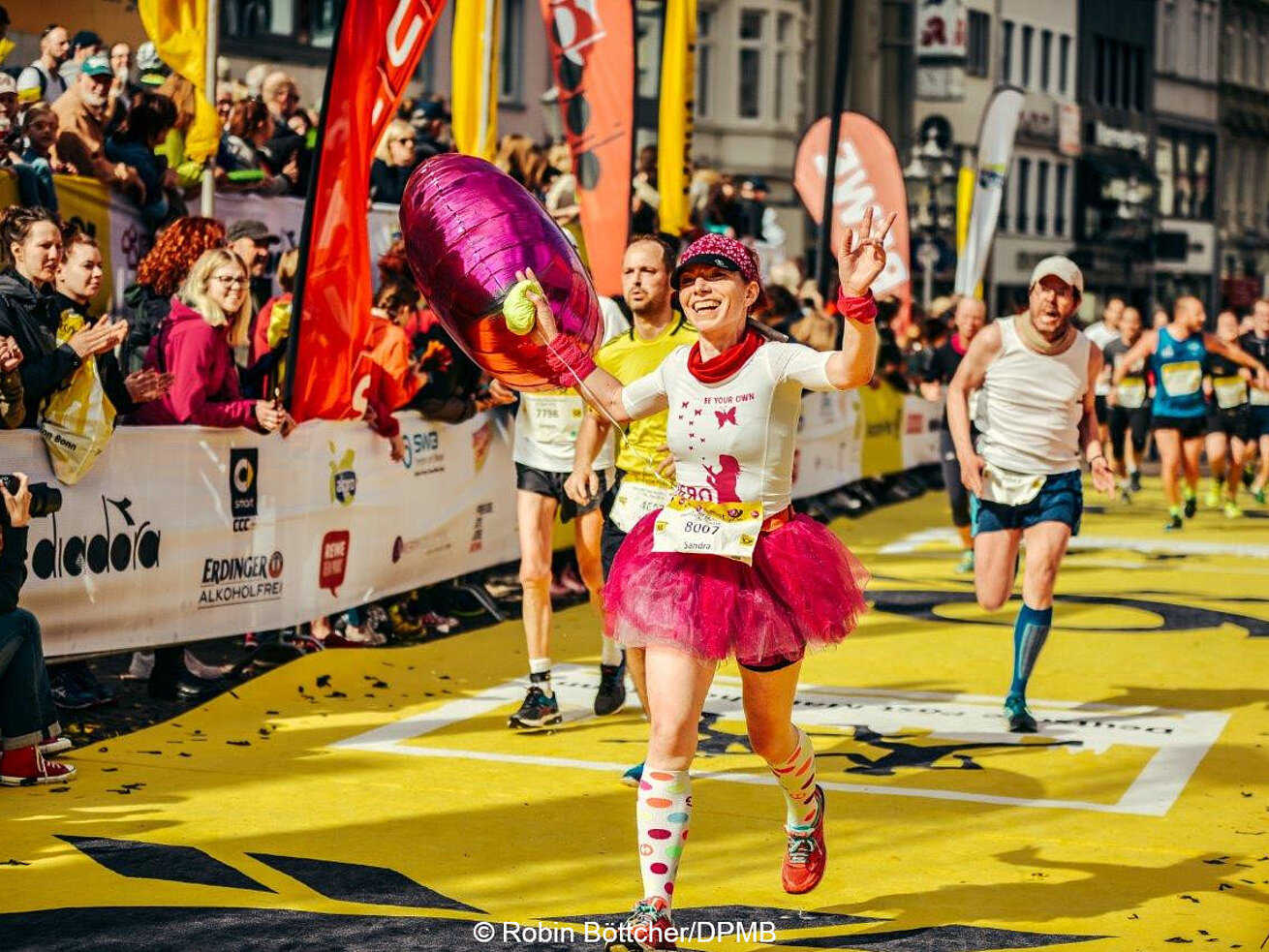 Female runner in pink outfit celebrates crossing the finish line at a city marathon