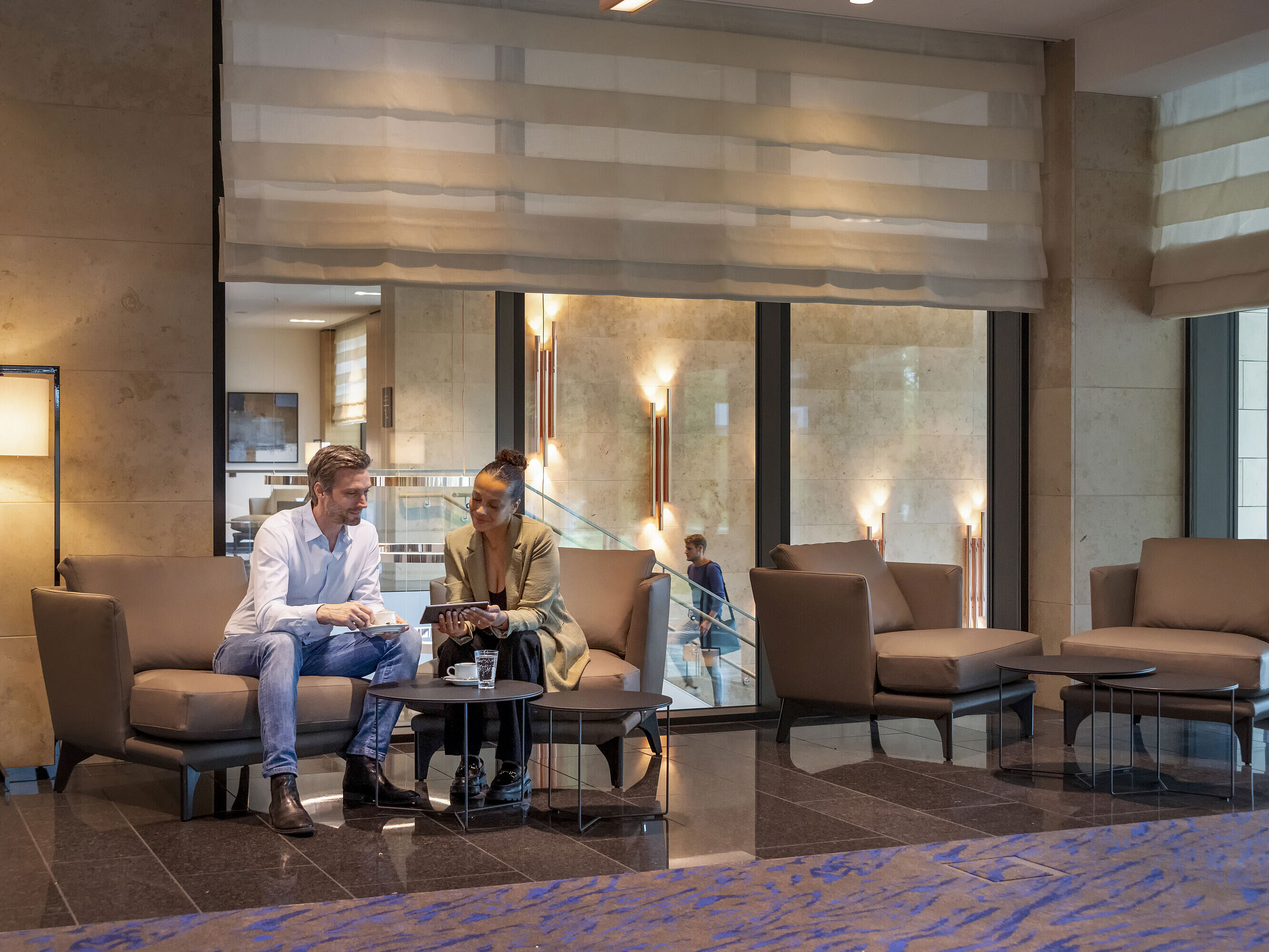 Man and woman sit in the Maritim Hotel Ingolstadt lobby, chatting over coffee.
