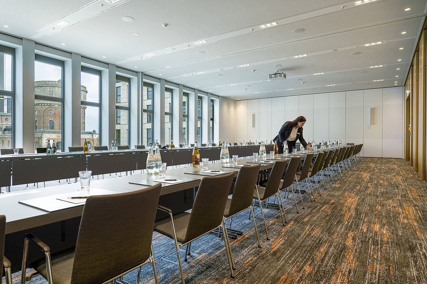 Employee setting up a modern meeting room at Maritim Hotel Ingolstadt. Large windows with city view.