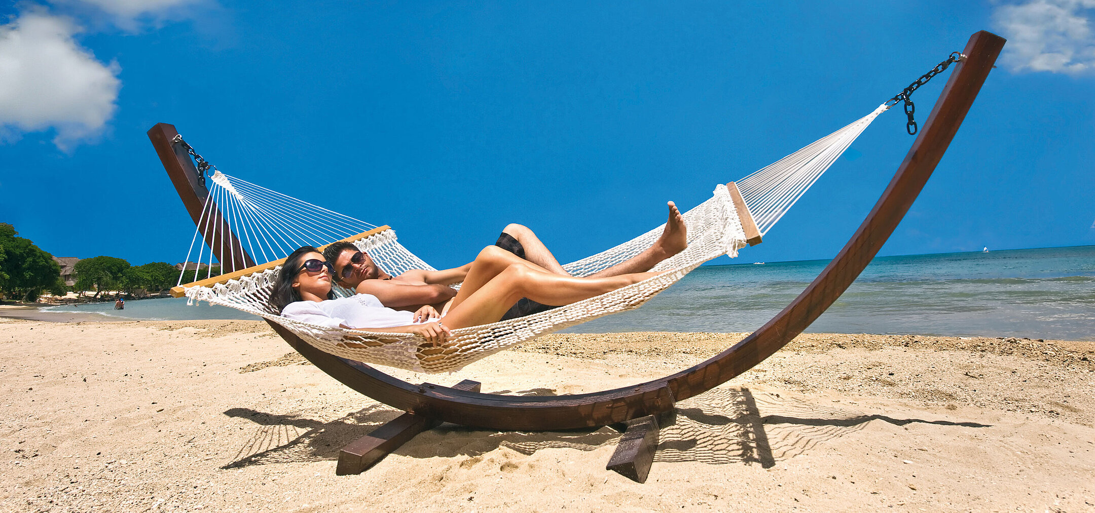 Couple relaxing in a hammock on a sandy beach with view of the blue sea