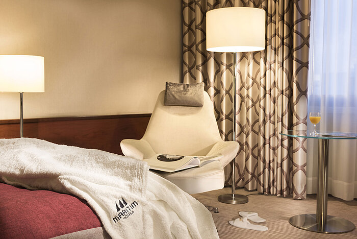 Detail of a Comfort room at Maritim Hotel Bonn with armchair, table, juice glass, and bathrobe on the bed.