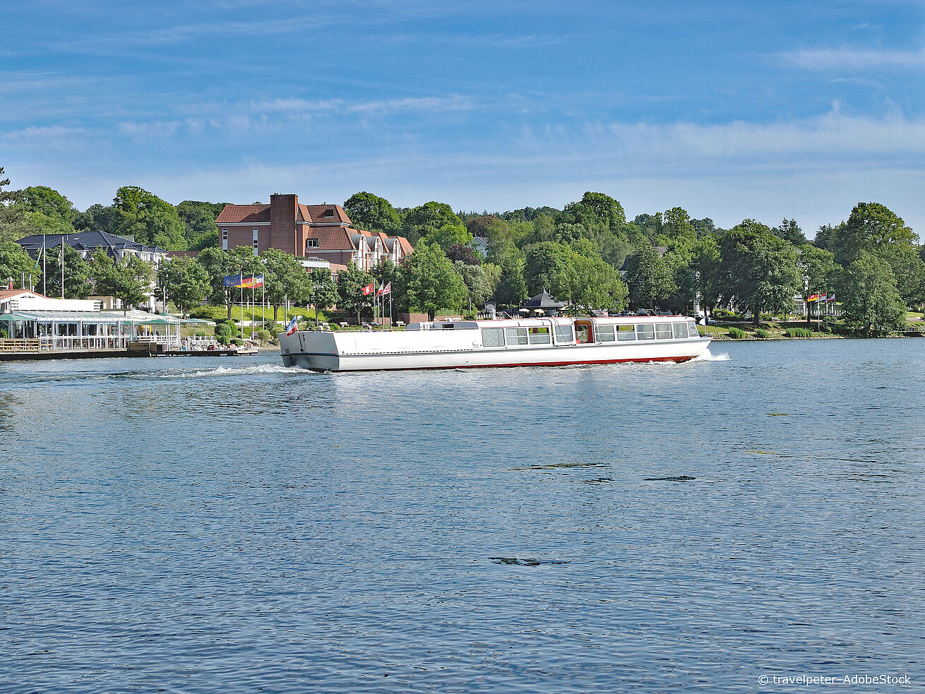 Excursion boat on a lake in the Holstein Switzerland region, surrounded by green shores, trees and a blue summer sky