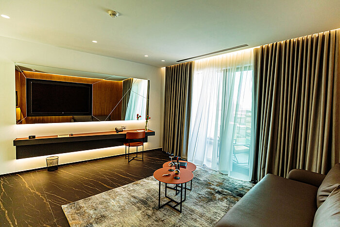 Bright living area at Maritim Resort Marina Bay with sofa, TV and floor-to-ceiling window