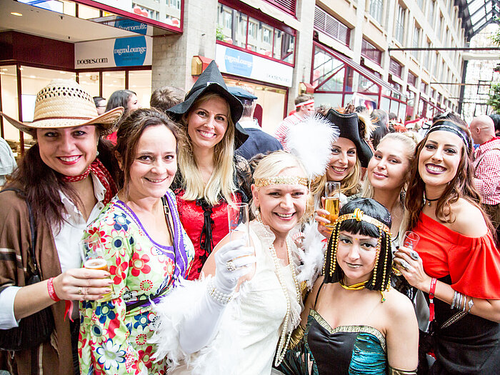 Women in colorful costumes celebrate at a carnival and hold champagne glasses up to the camera.