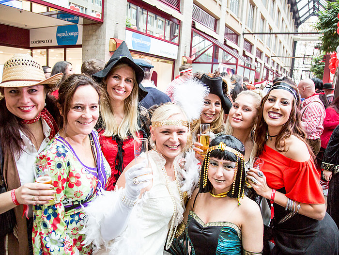 Women in colorful costumes celebrate at a carnival and hold champagne glasses up to the camera.